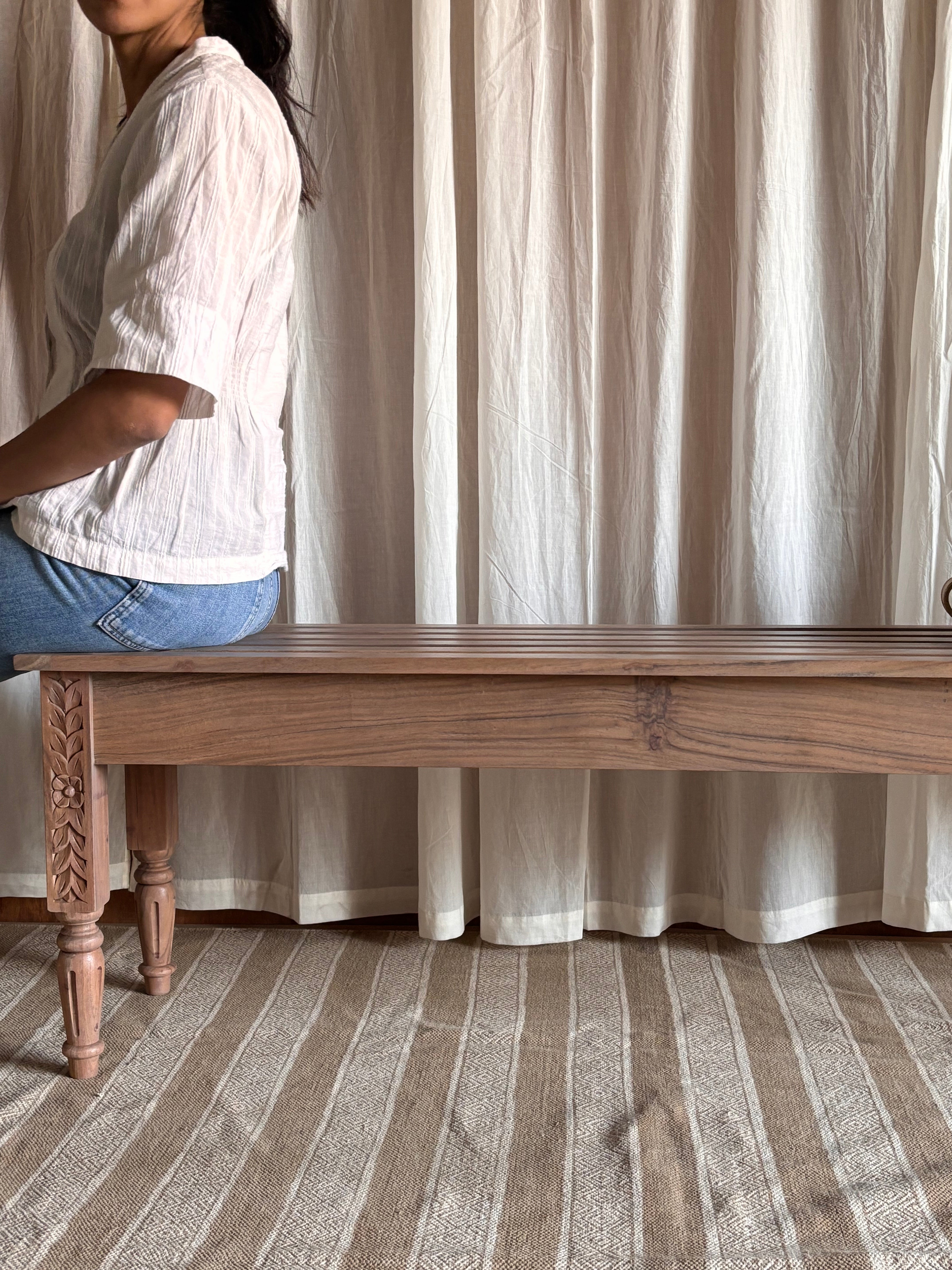 Person sitting on a decorative wooden bench with a curtain background