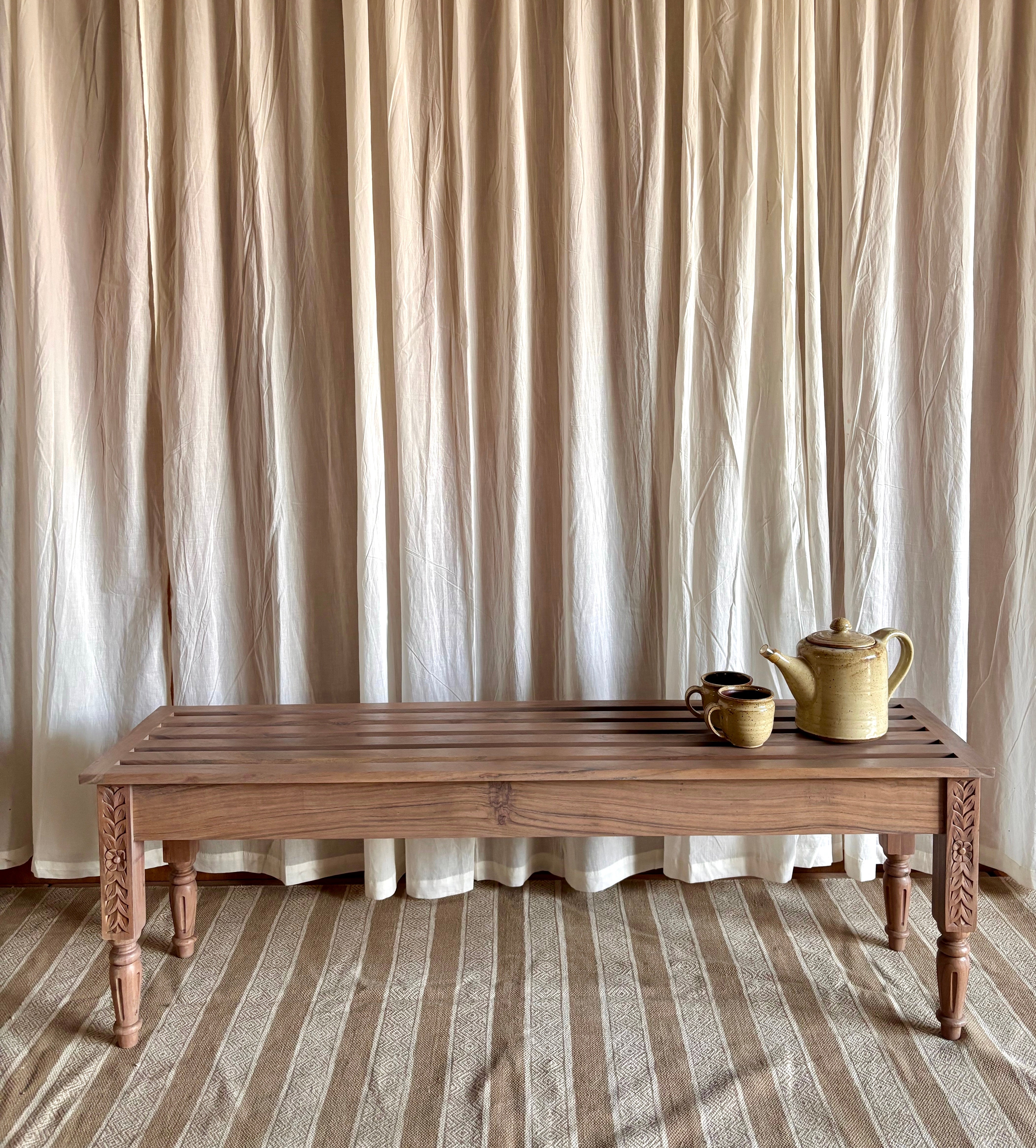 Wooden bench with a teapot and cups against a curtain backdrop