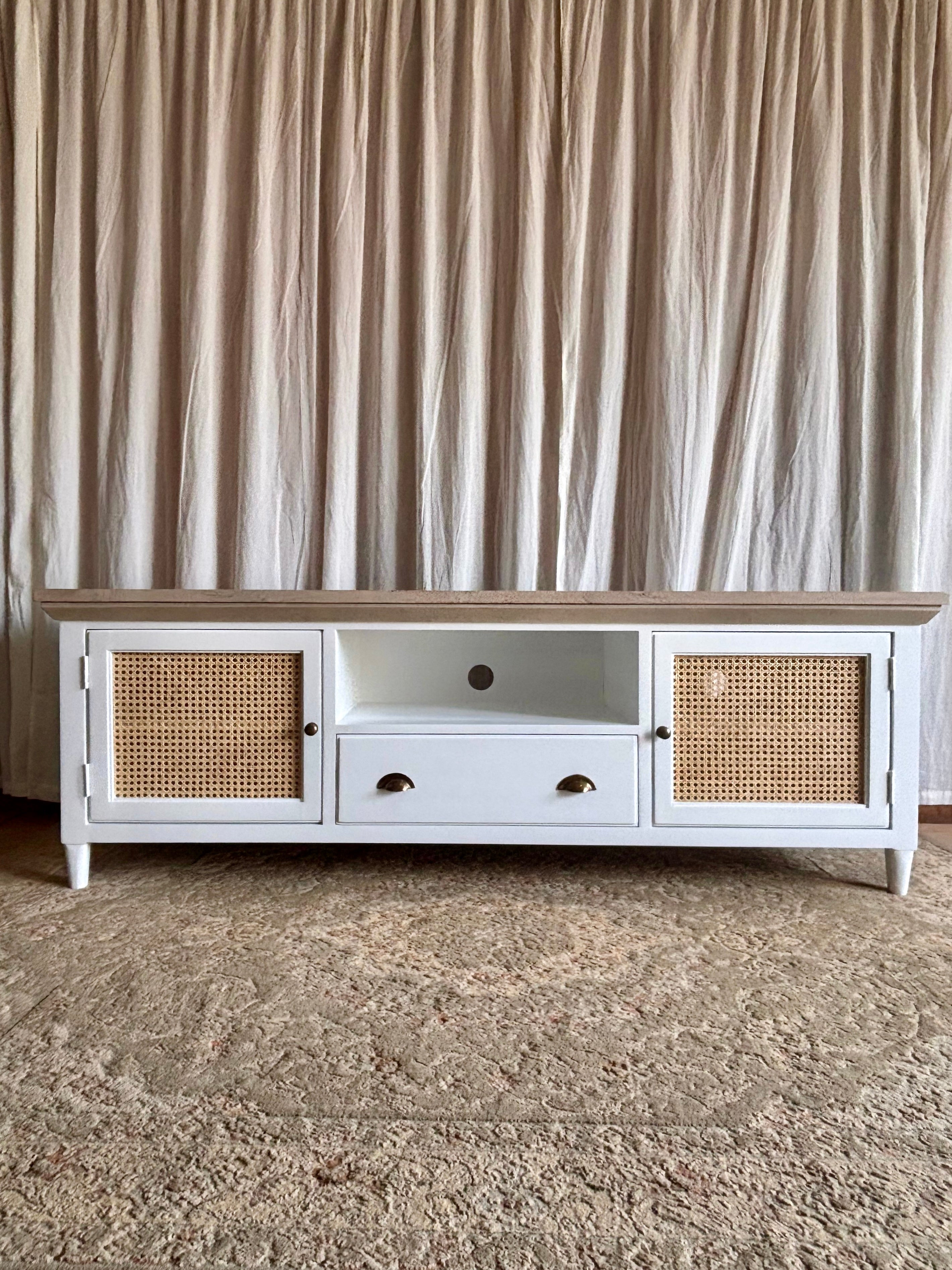 White TV stand with wicker doors against a beige curtain background