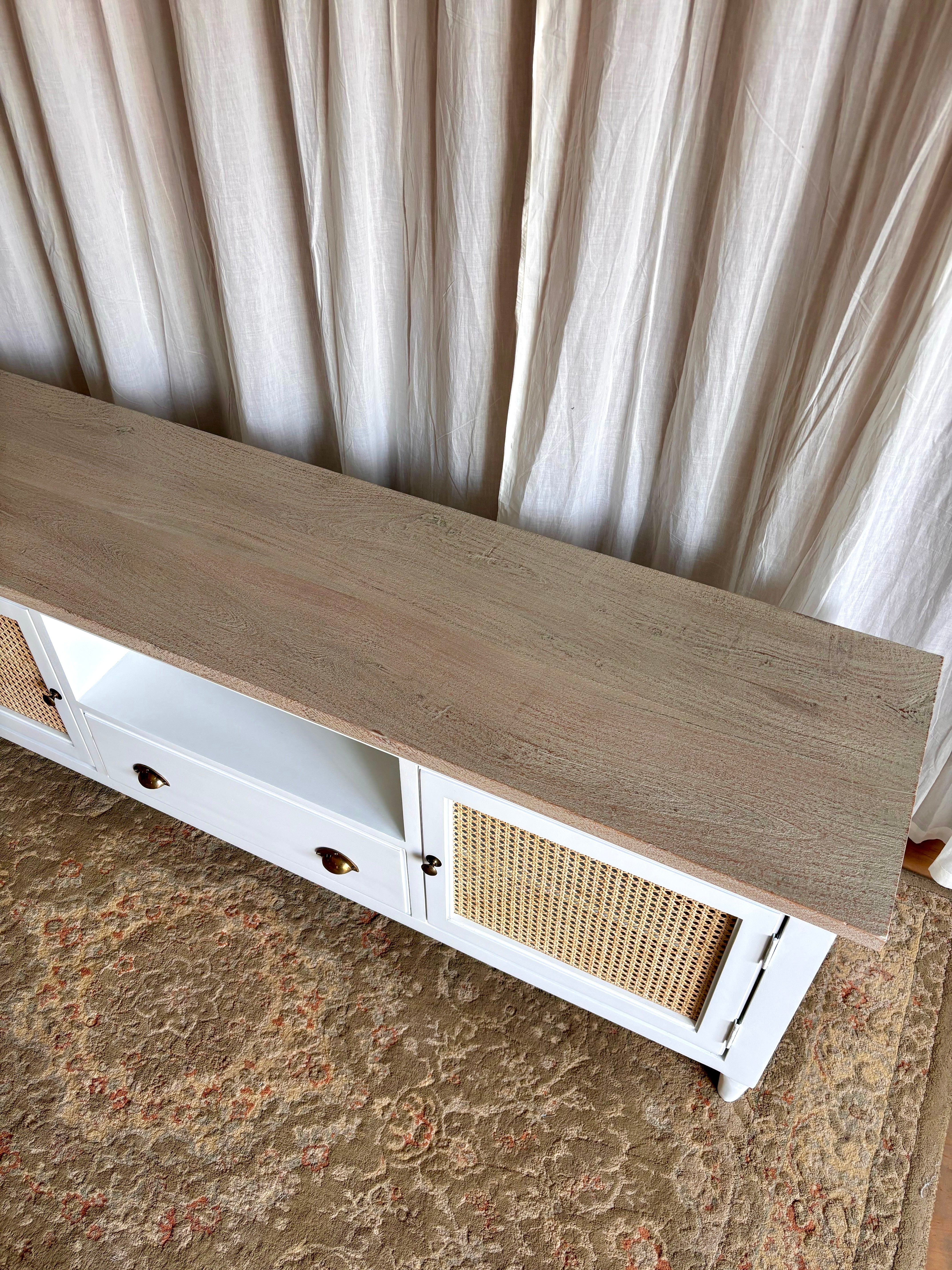 Wooden TV unit table with wicker accents against a curtain backdrop