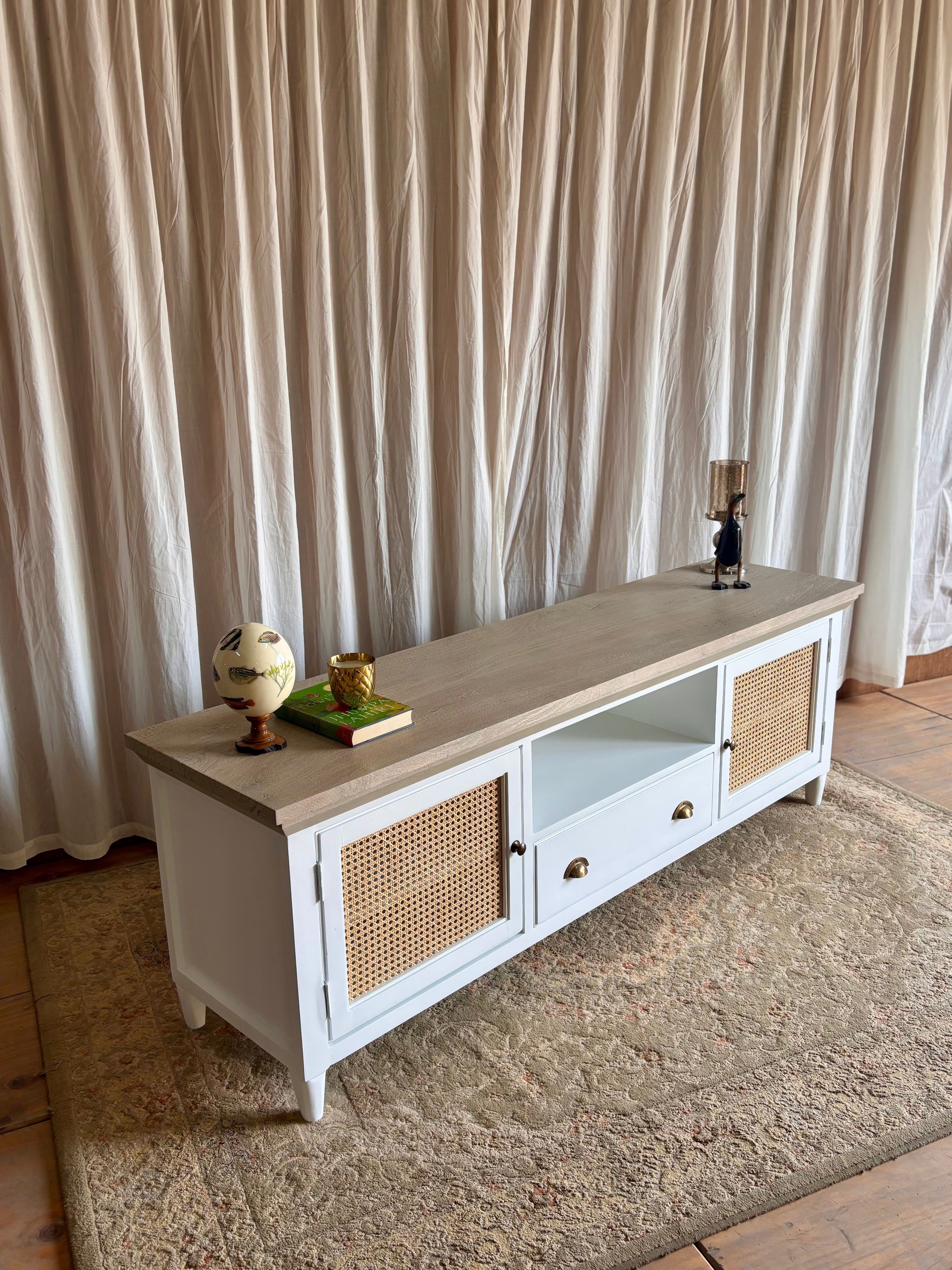 Long wooden TV unit table with decorative items against a curtain backdrop